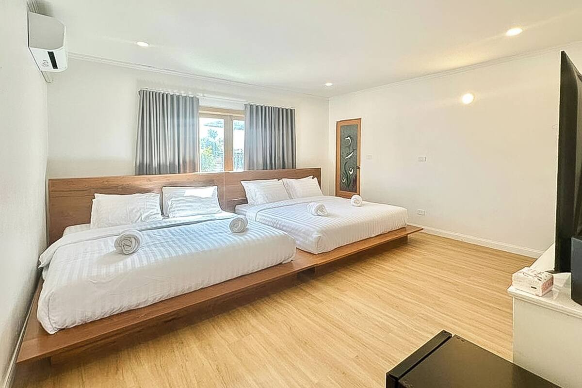 Habitación doble con dos camas, cabecera de madera, ventana con cortinas, televisor montado en la pared y suelo de madera.