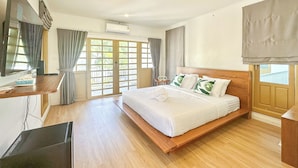 Una habitación de hotel con una cama grande, piso de madera, un escritorio con teléfono, un televisor y una ventana con cortinas.