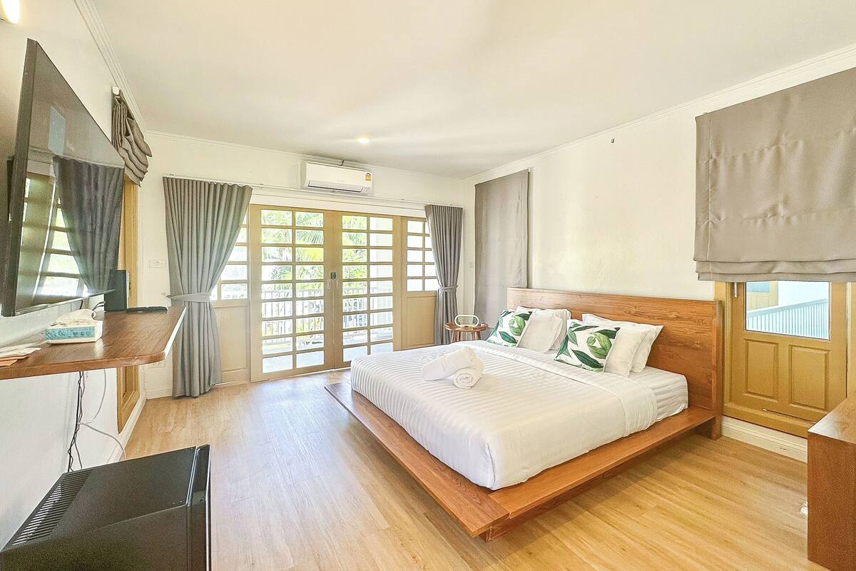 Una habitación de hotel con una cama grande, piso de madera, un escritorio con teléfono, un televisor y una ventana con cortinas.