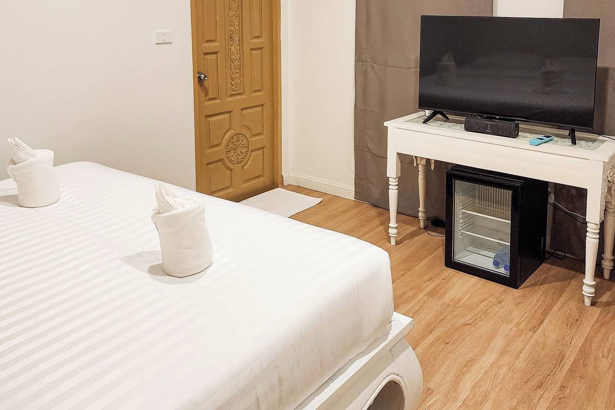 Una habitación de hotel con una cama, un televisor sobre un mueble, una puerta y un refrigerador pequeño.