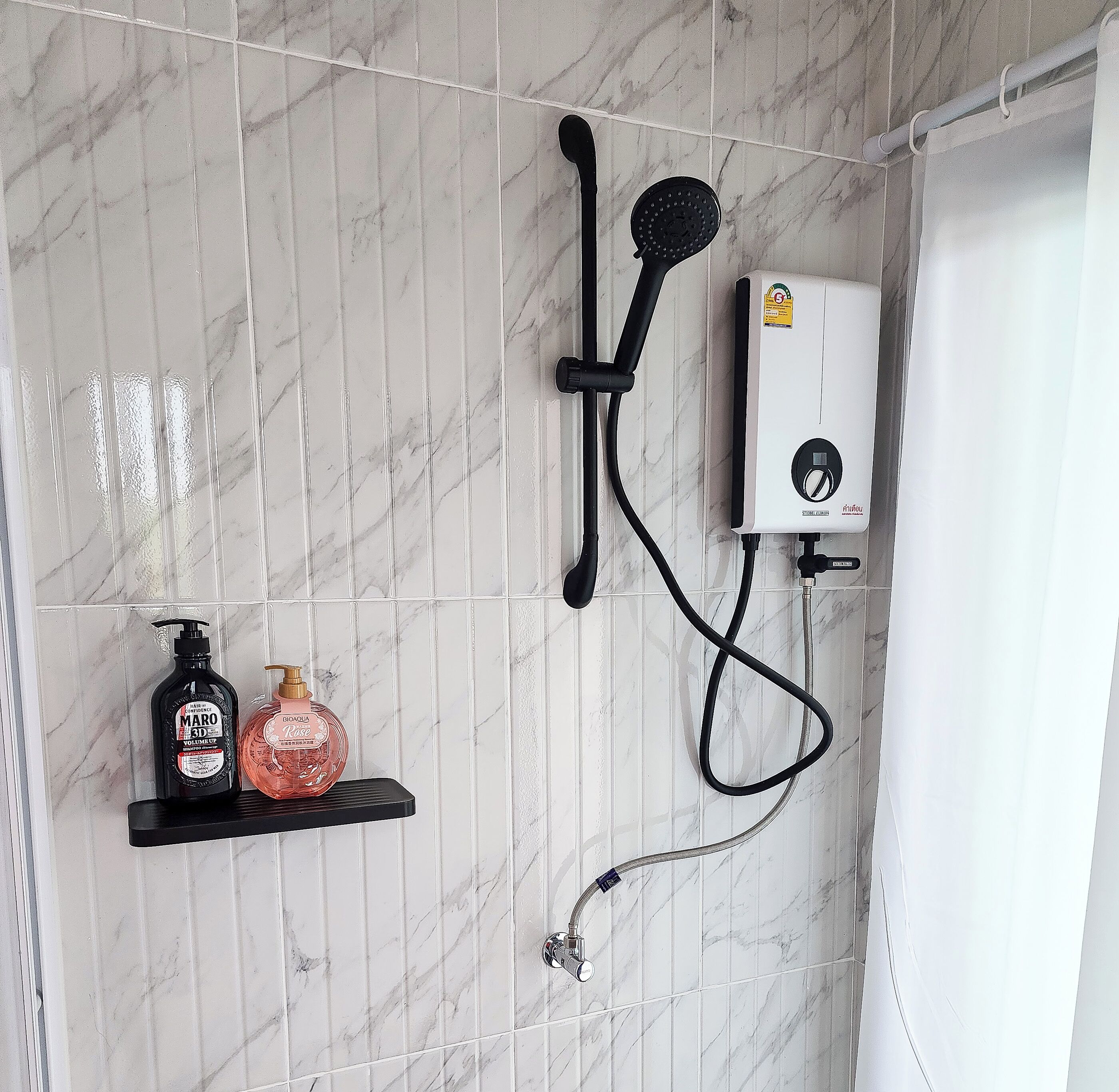 Ein Badezimmer mit Dusche, Duschbrause, Wandheizung und Ablagefläche mit zwei Shampoo- und Conditionerflaschen.