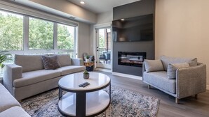 A modern living room with a sofa, armchair, coffee table, fireplace, and large windows. - Serenity at Sparrowhawk Lodge Brand New 2Bd 2Ba (Dead Man's Flats)