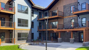 A multi-story building with balconies, a clear sky, and a well-maintained lawn. - Serenity at Sparrowhawk Lodge Brand New 2Bd 2Ba (Dead Man's Flats)