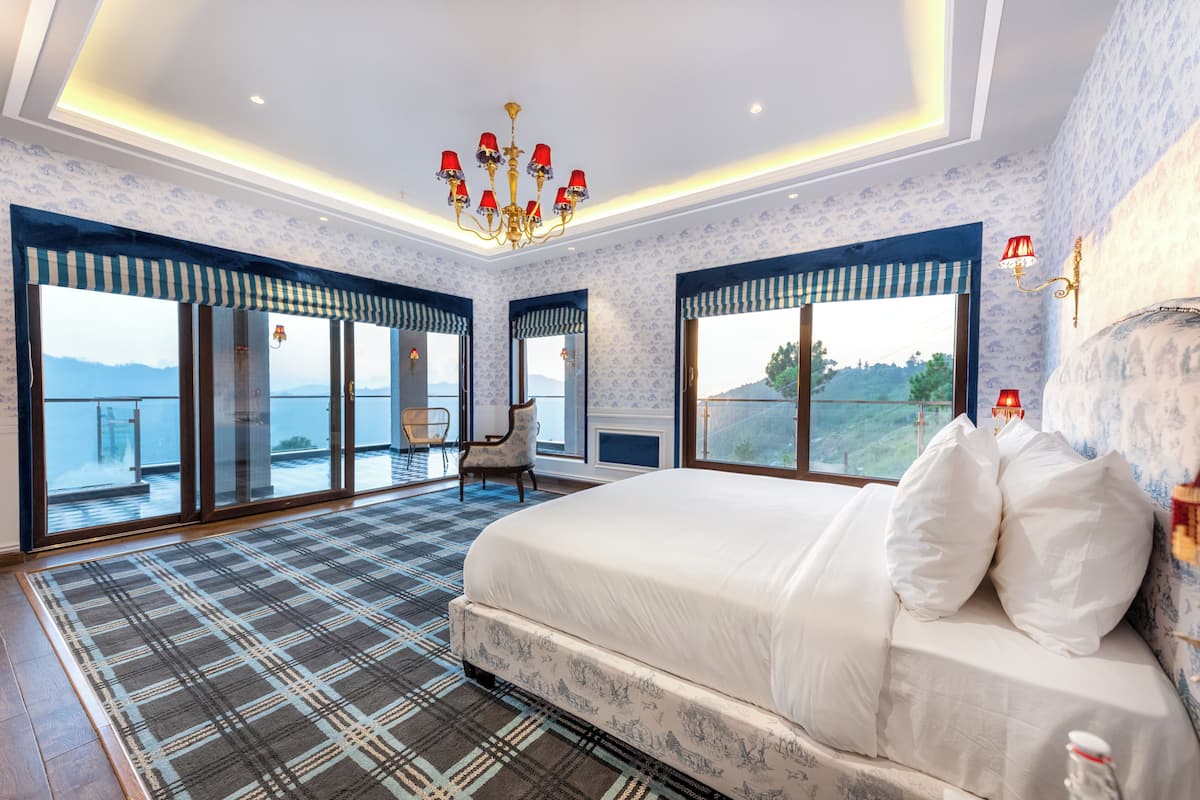 A spacious bedroom with a large bed, a chandelier, and a view of the sea.