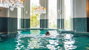 A swimming pool with a person swimming, surrounded by large windows and a chandelier. - The Manor Wellness & Sport Hotel (Shimla)