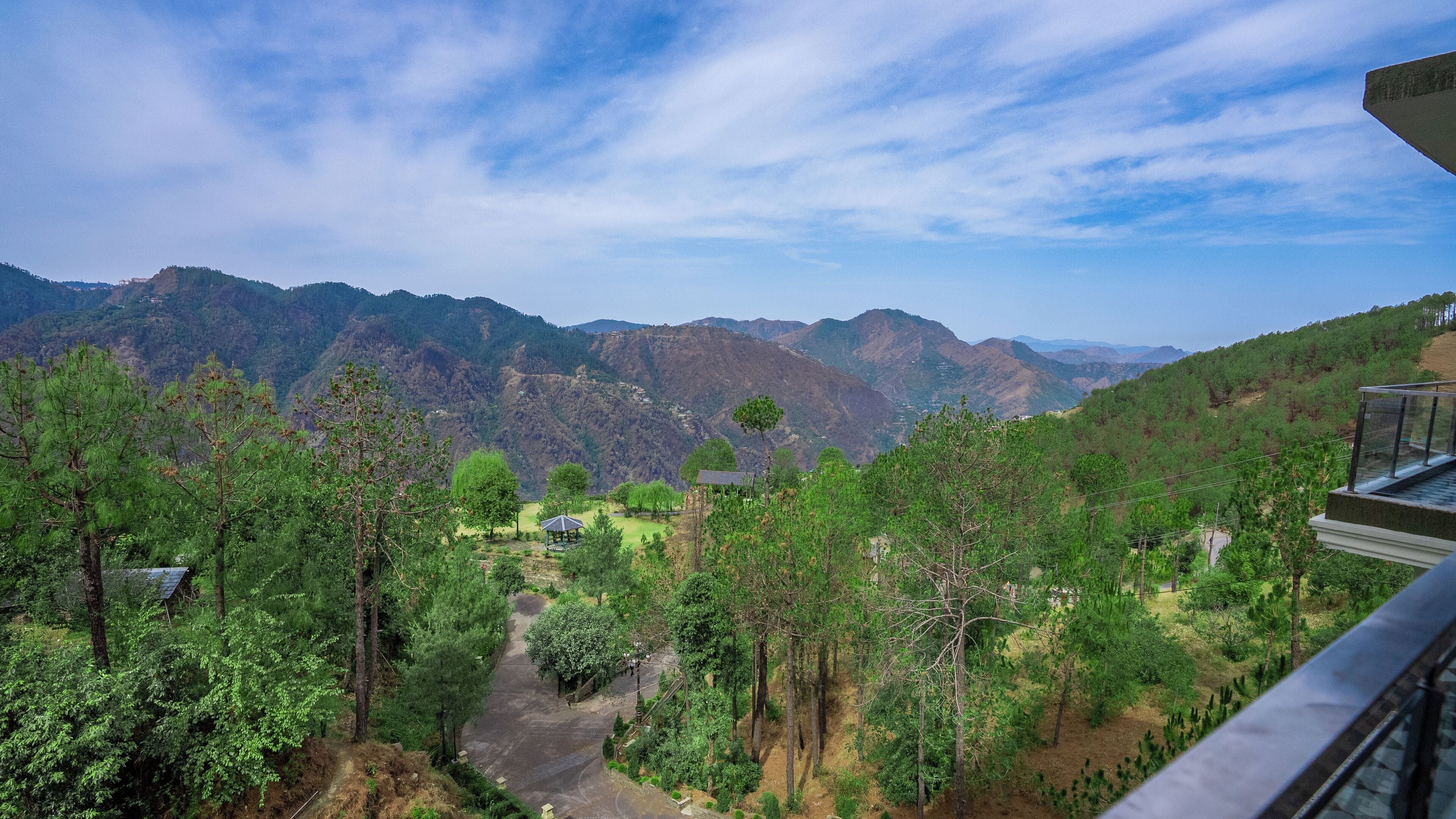 A mountainous landscape with a clear sky. There are trees and a small building visible.