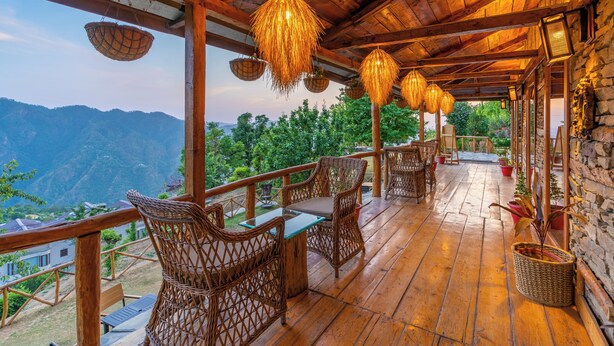 A wooden deck with wicker furniture and hanging baskets, overlooking a mountainous landscape. - The Manor Wellness & Sport Hotel (Shimla)