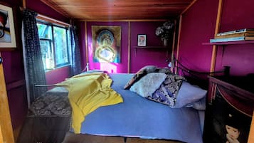 A room with a bed, a window with curtains, a painting on the wall, and a shelf with books.