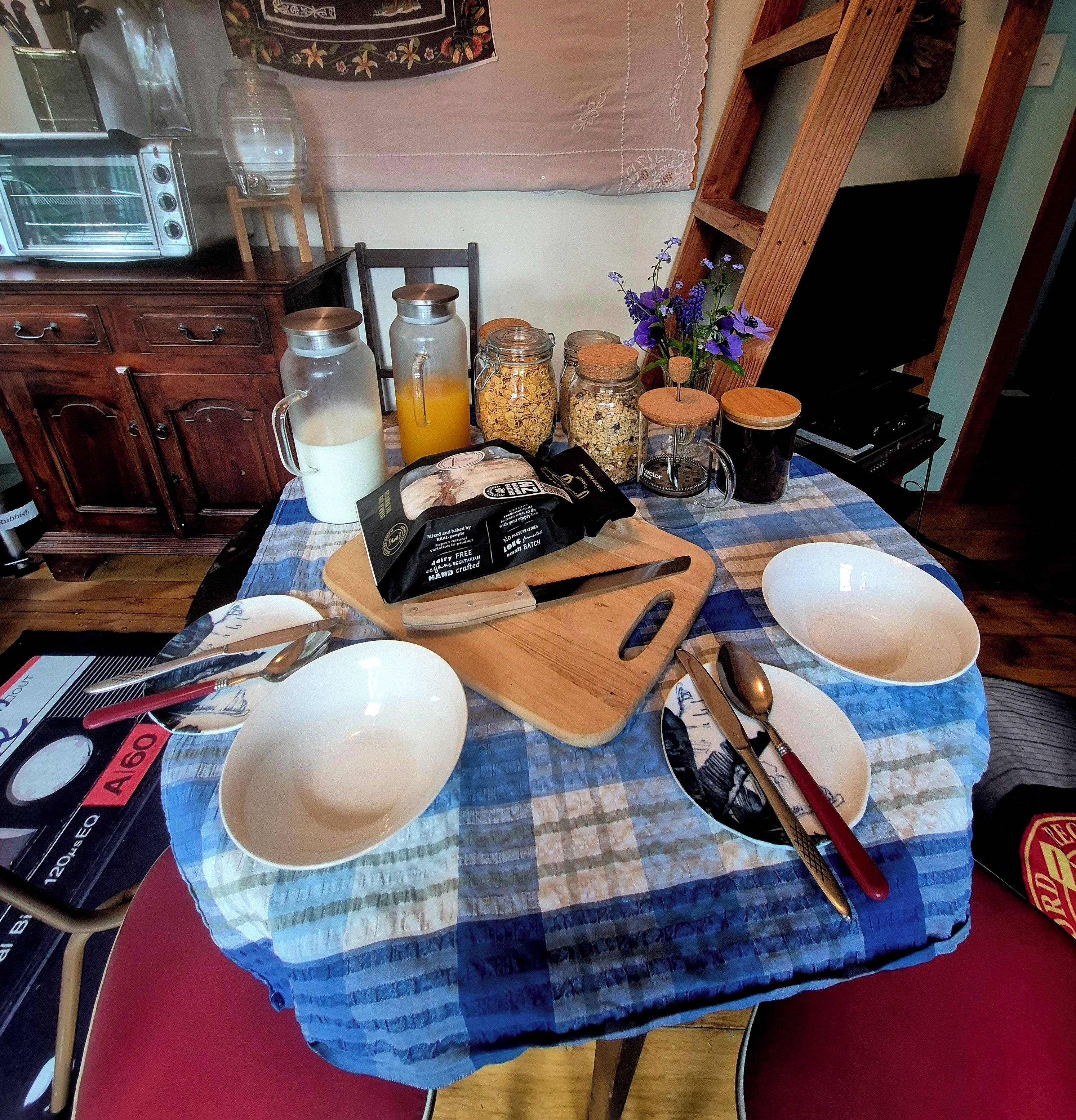 Una mesa de cocina con mantel a cuadros, una tabla de cortar con alimentos y diversos utensilios de cocina.