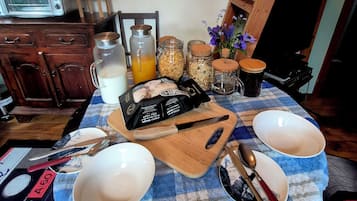 Una mesa de cocina con mantel a cuadros, una tabla de cortar con alimentos y diversos utensilios de cocina.