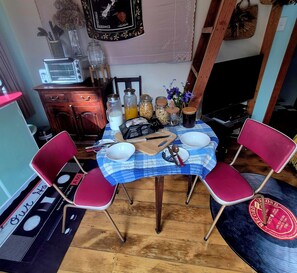 A dining area with a table set for two, surrounded by red chairs, a blue tablecloth, and various kitchen items.