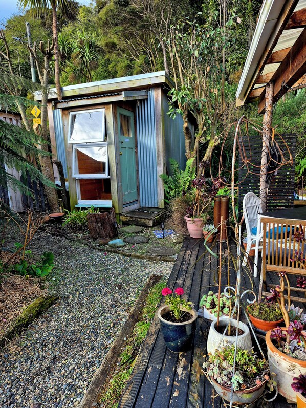 A rustic outdoor area with a wooden deck, potted plants, and a small shed.