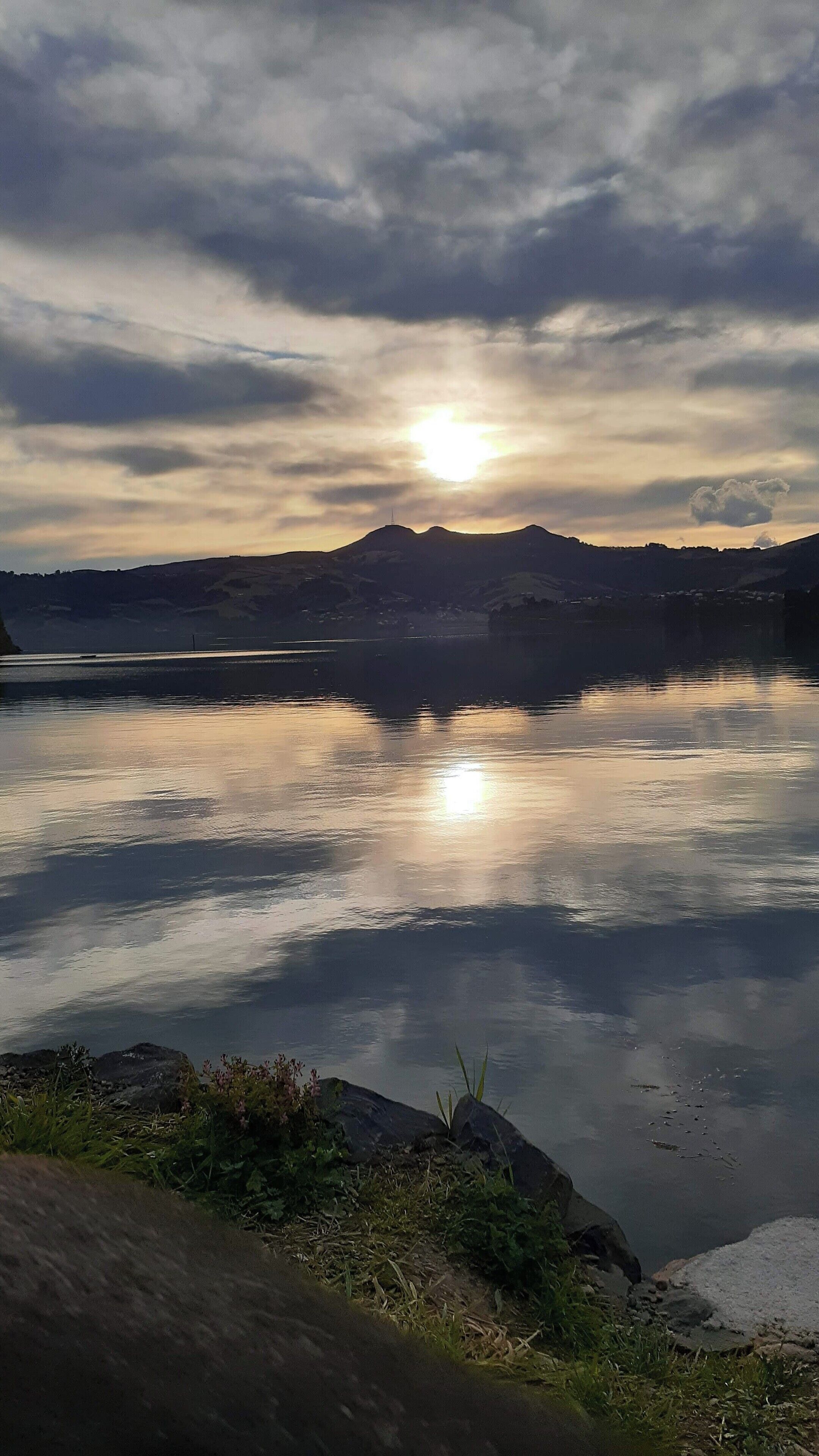 Ein ruhiger See mit einem Berg im Hintergrund und bewölktem Himmel.