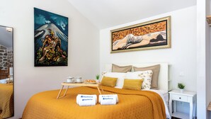 A hotel room with a large bed, two paintings on the walls, a bedside table with a plant, and two towels with the 'hostwise' logo.