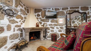 A stone-walled room with a fireplace, a television mounted on the wall, and a plaid-patterned sofa.
