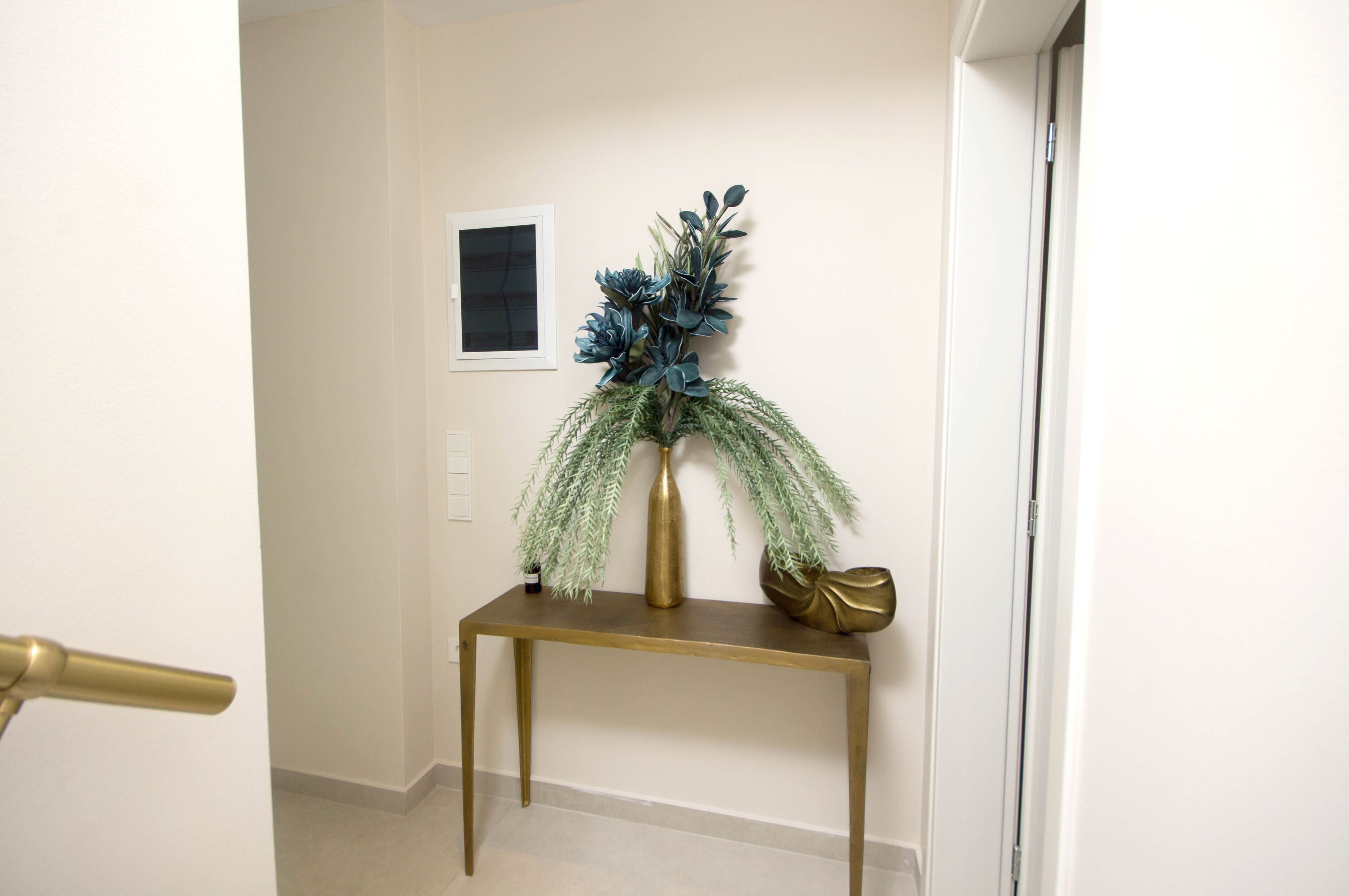 A hallway with a gold console table, a vase with green foliage, and a small framed picture on the wall.