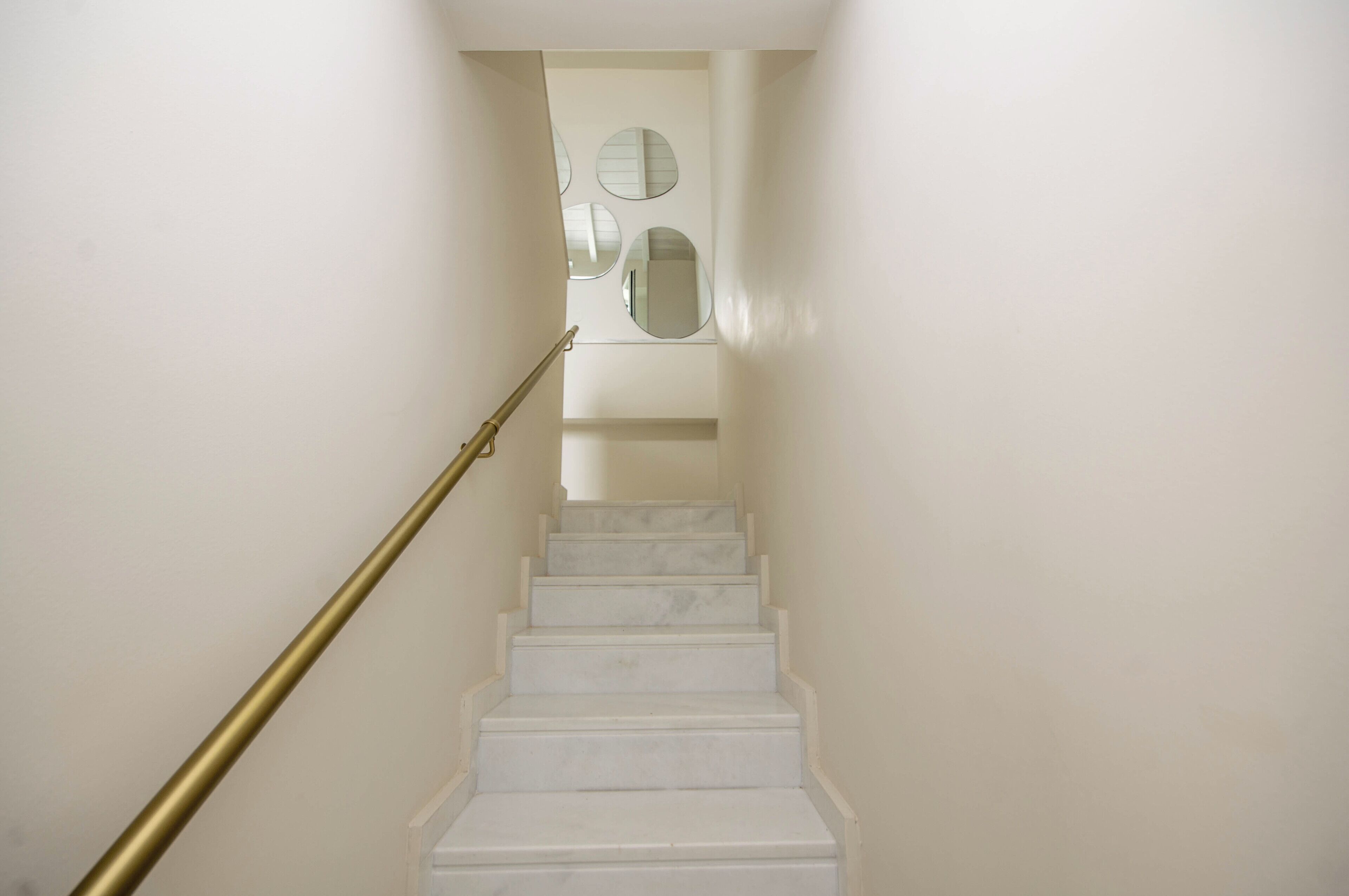 A staircase with white marble steps and a brass handrail, leading to a landing with three round mirrors.