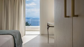 Ett hotellrum med en säng, ett bord och utsikt över havet genom ett stort fönster.