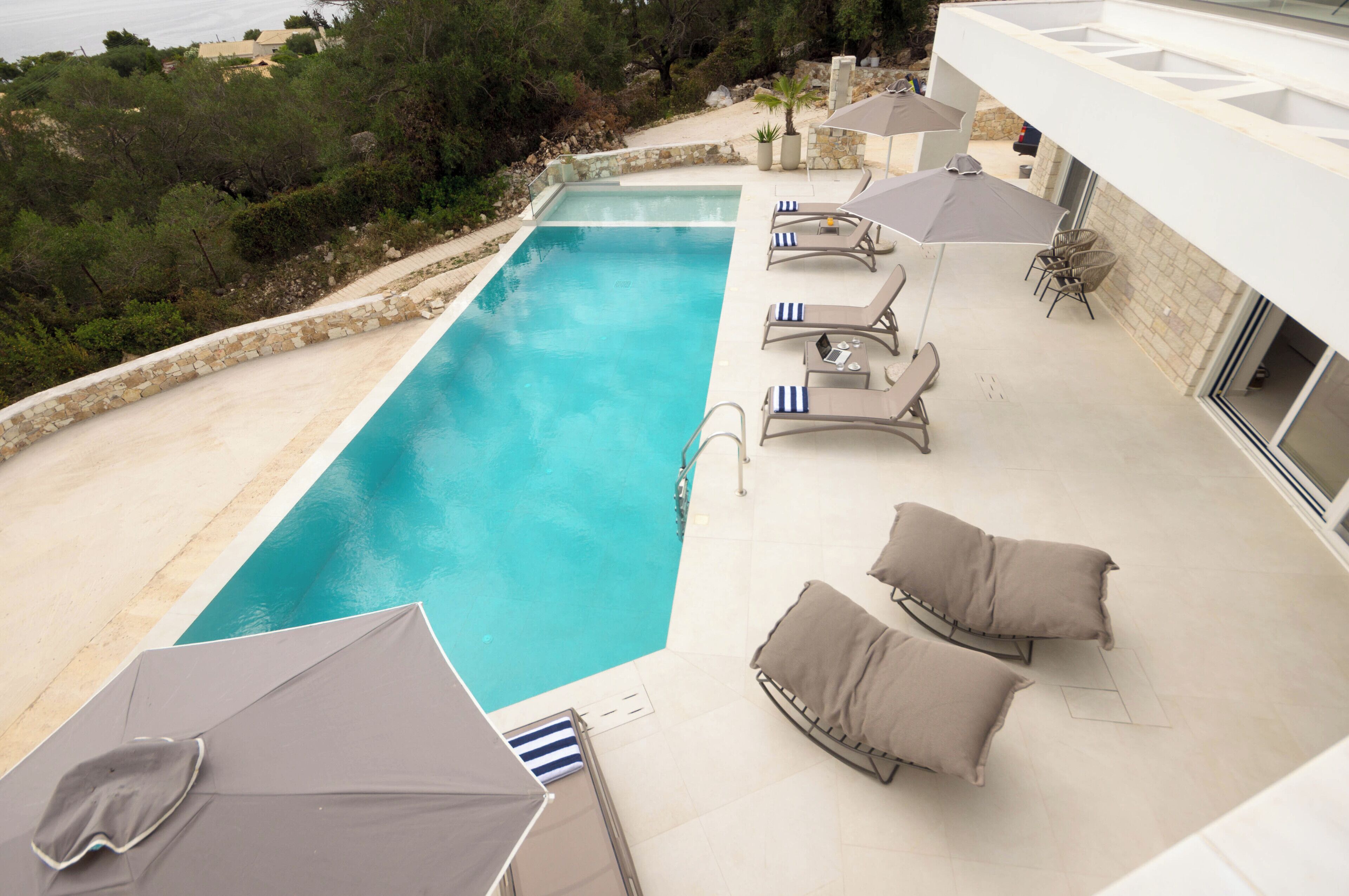 Ein rechteckiger Pool mit Steinrand, umgeben von Liegestühlen und Sonnenschirmen.