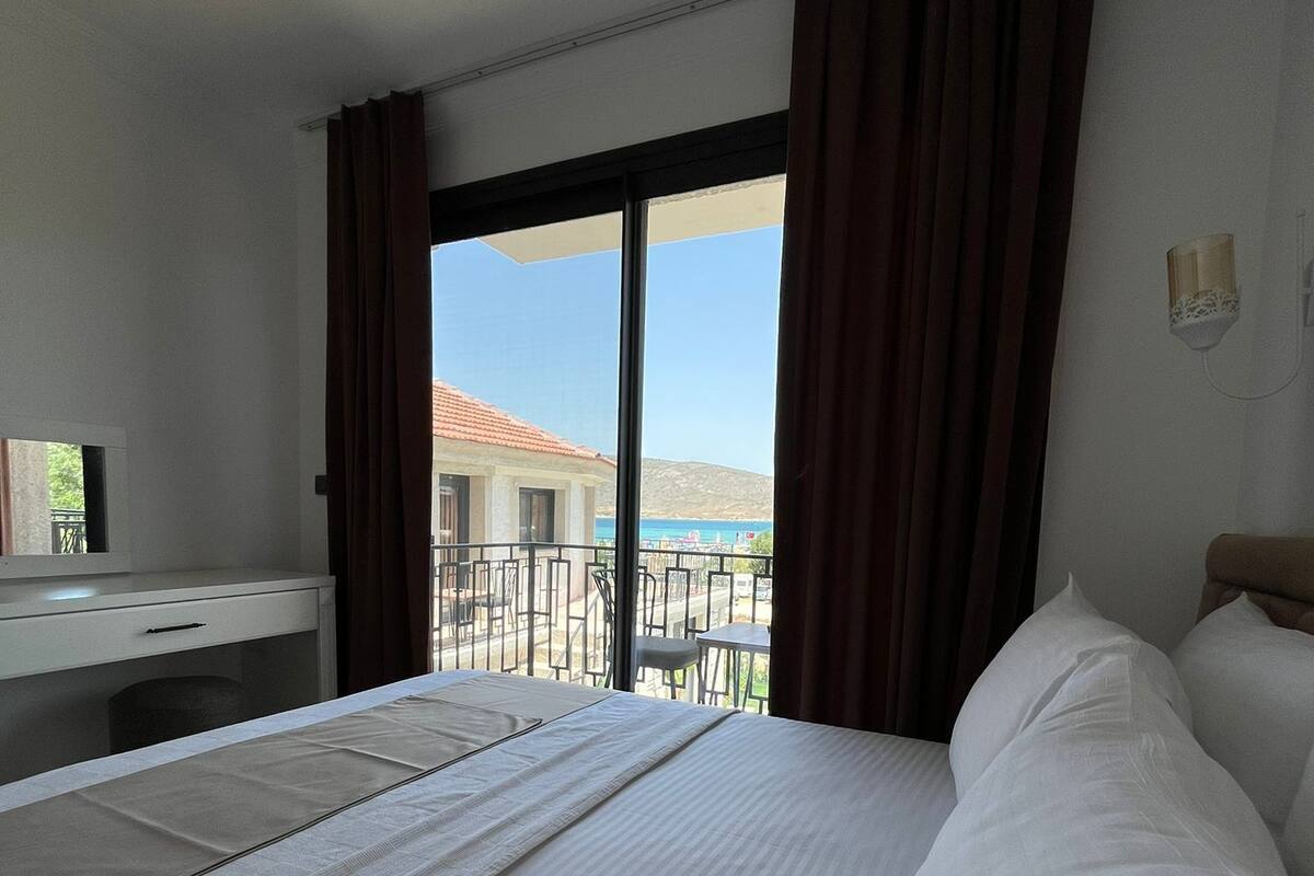 A hotel room with a bed, a desk, and a view of the sea and buildings.