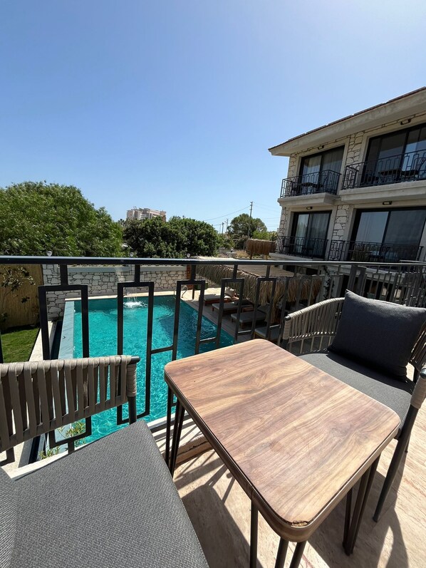 A rooftop pool area with a table and chairs, a stone wall, and a building with balconies in the background. - Lotus Port  (Cesme)