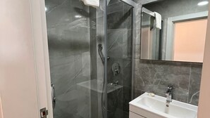 A modern bathroom with a glass-enclosed shower, a white sink, and a large mirror. - Lotus Port  (Cesme)