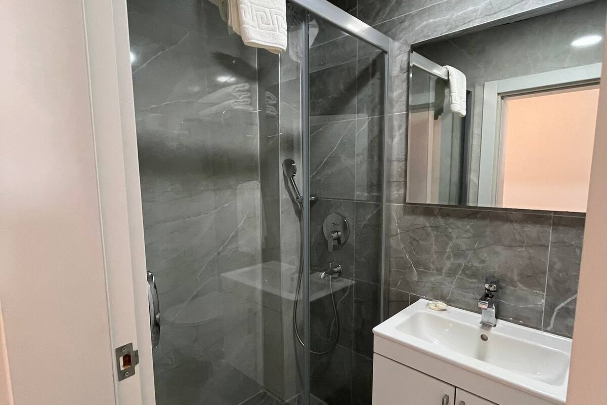 A modern bathroom with a glass-enclosed shower, a white sink, and a large mirror.