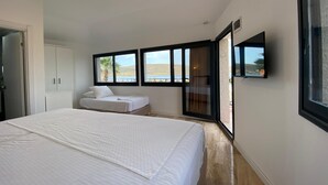 A bedroom with a large bed, a wardrobe, a TV, and a view of the outdoors through windows. - Lotus Port  (Cesme)