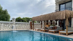 A swimming pool with a stone wall and a thatched roof seating area. - Lotus Port  (Cesme)