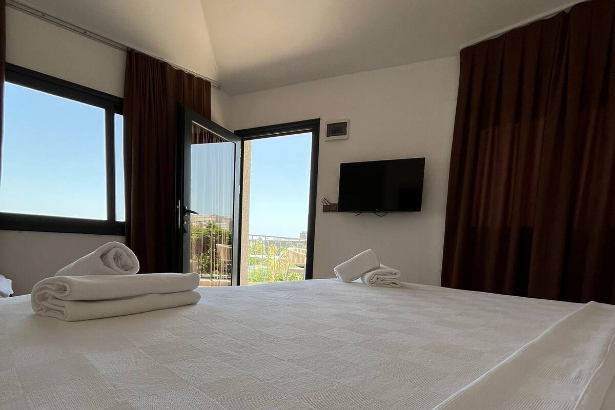 A hotel room with a large bed, a flat-screen TV mounted on the wall, and a balcony with a view.