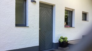 A building with a white exterior, a dark grey door, and a small potted plant near the entrance. - Urlaub Inmitten der Natur (Mechernich)