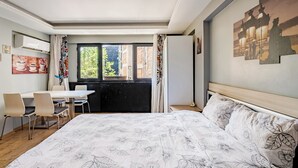 Un dormitorio con cama, escritorio, sillas, una ventana y obras de arte en las paredes.