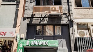 A multi-story building with air conditioning units, a storefront with a green sign, and a visible window with a curtain. - Cozy Central Flat w/Netflix & Elevator Near Metro 2 minute walking distance (İstanbul)