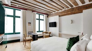 A hotel room with a large bed, a desk, a chair, and a TV mounted on the wall.