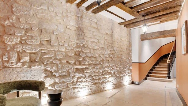 A stone-walled hallway with a wooden ceiling, a staircase, and a chair.