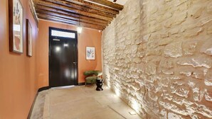A hallway with a stone wall, a black door, and a small table with a bowl.