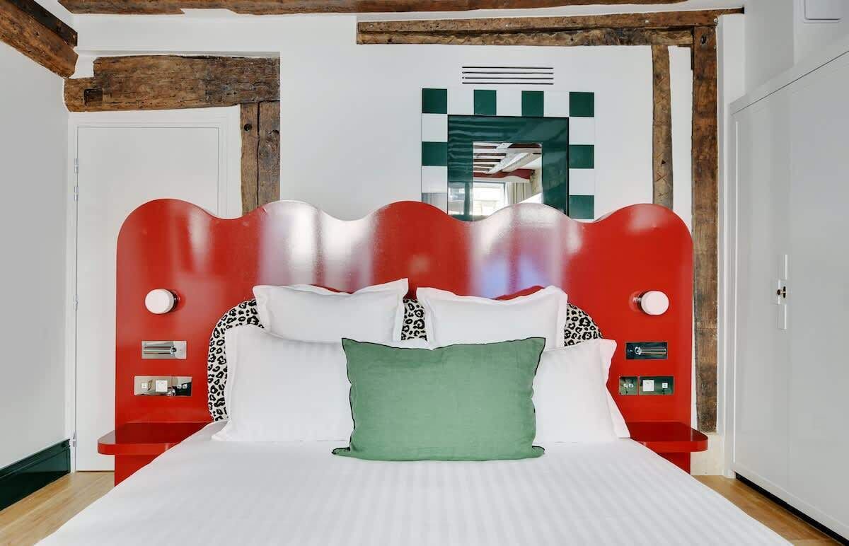 Ein modernes Schlafzimmer mit einem roten Kopfteil, weißer Bettwäsche und einem grünen Kissen.