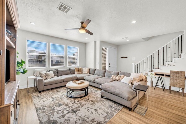 Spacious living room in Washington, Utah short-term rental with large sectional sofa, modern ceiling fan, and natural light through wide windows near St. George.