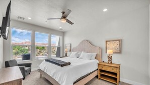 Quarto com cama, escrivaninha, cadeira, mesa de cabeceira, abajur e ventilador de teto.