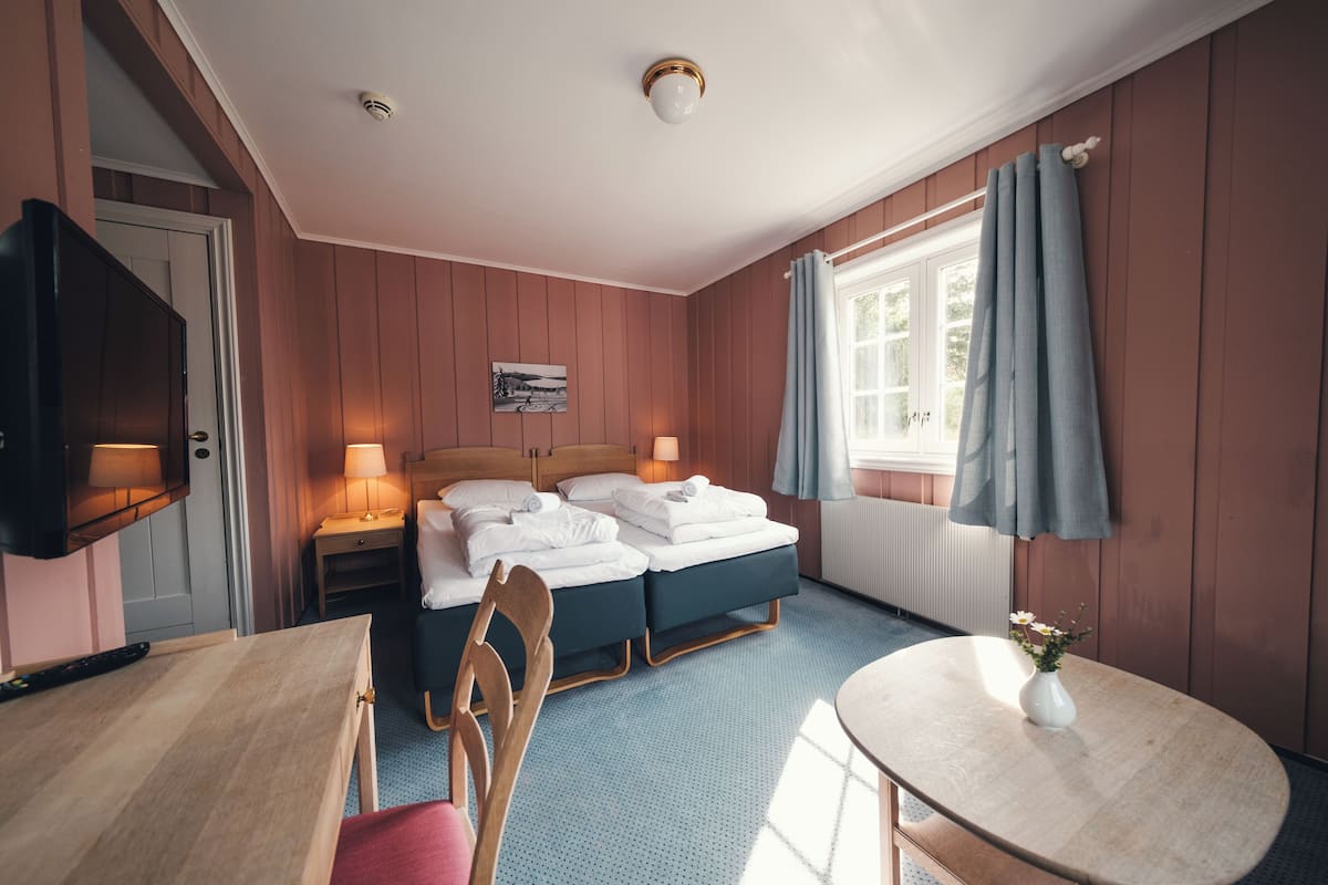 A hotel room with a bed, bedside tables, a TV, a chair, a table, and a window with curtains.