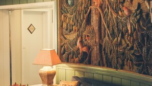 Una sala de estar acogedora con un sofá azul, una mesa de centro de madera, una lámpara y un mural decorativo en la pared.
