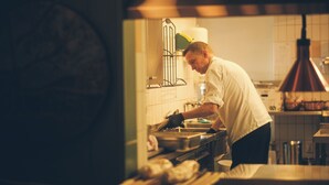 Un chef trabajando en una cocina con salpicadero de azulejos, electrodomésticos de acero inoxidable y una lámpara colgante de cobre.