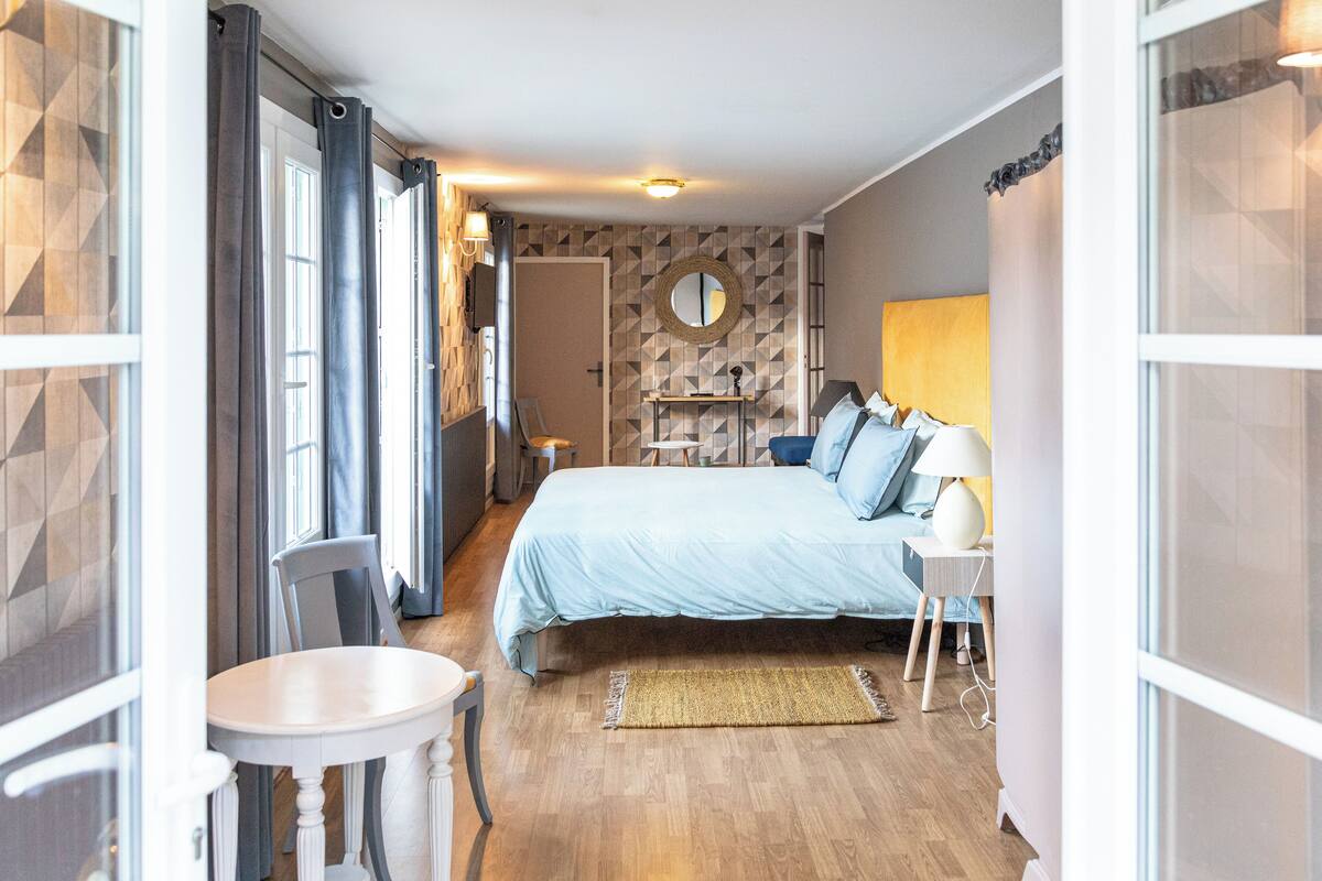 A bedroom with a bed, bedside table, lamp, and a mirror on the wall.