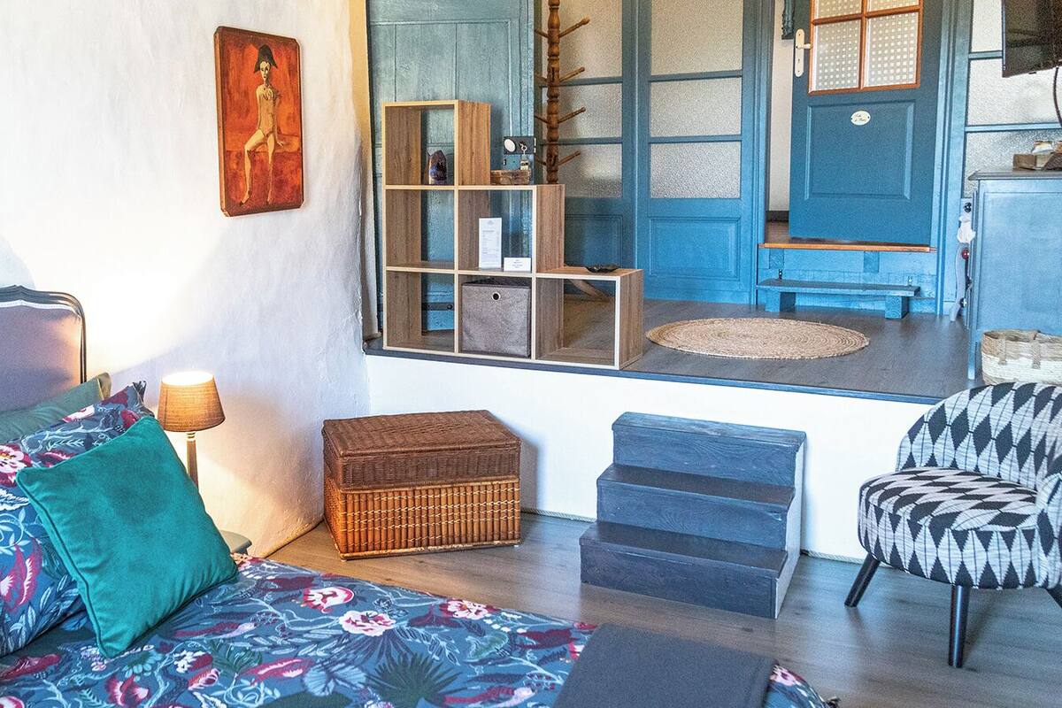 A cozy living room with a sofa, cushions, a lamp, a wicker basket, a chair, and a view of the outside.
