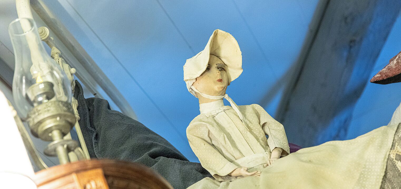 Een pop met een muts en jurk, geplaatst op een bed.