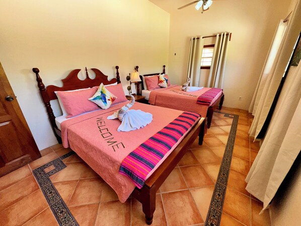 Une chambre d’hôtel avec deux lits, chacun agrémenté d’une pancarte « BIENVENUE », d’une tête de lit en bois et d’une couverture rayée aux couleurs vives.