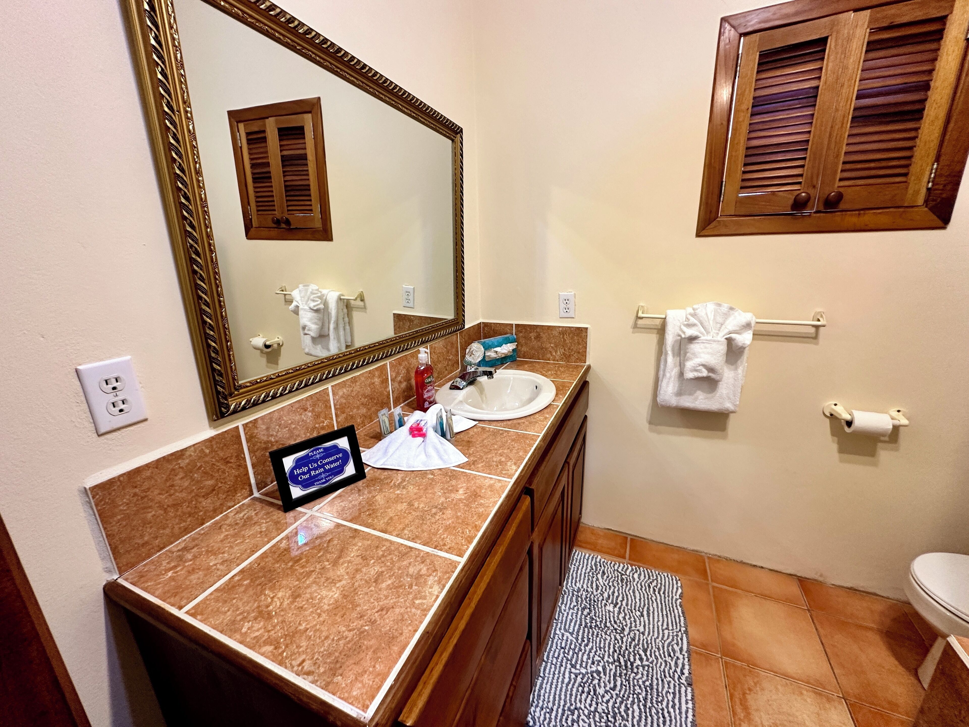A bathroom with a marble countertop, a sink, a mirror, a towel rack, and a toilet.