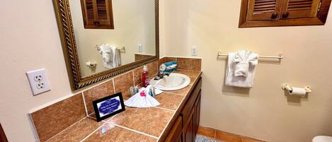 A bathroom with a marble countertop, a sink, a mirror, a towel rack, and a toilet.