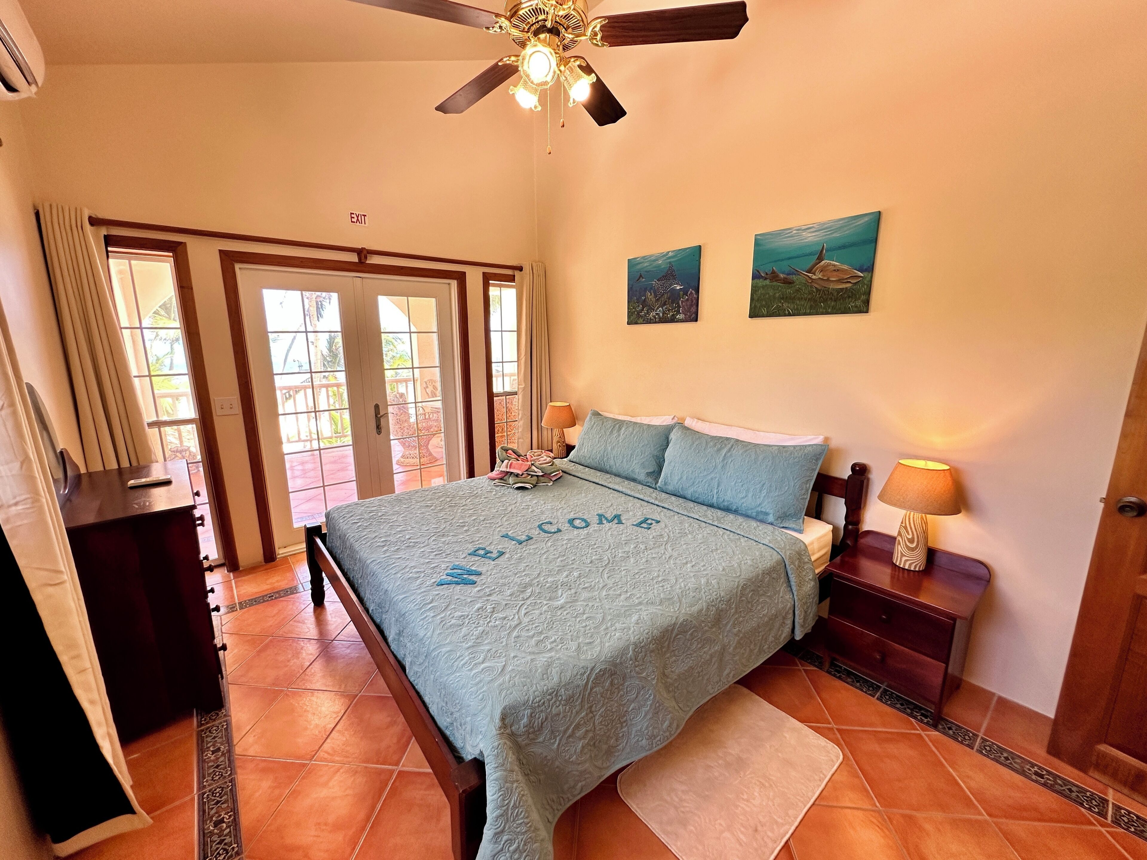 Quarto com cama, mesa de cabeceira, ventilador de teto e vista exterior por uma porta de correr.