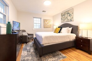 A bedroom with a bed, bedside tables, a desk, a chair, and artwork on the walls.